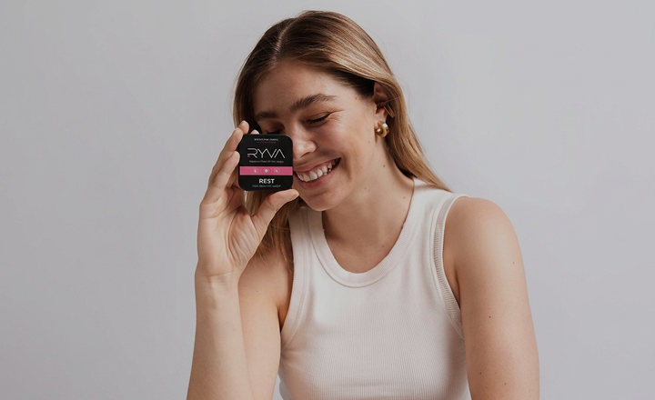 Woman holding a black container with 'RYVA' branding against a plain background