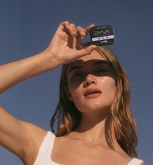 Woman holding a small container labeled 'RYVA' against a clear blue sky